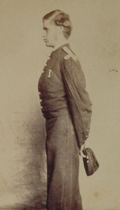 Young man in Civil War uniform standing in profile holding hat in hands behind back