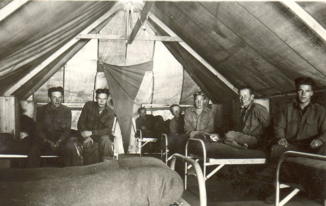 Old photo of men inside a tent sitting on cots.