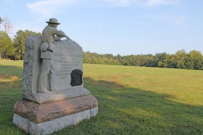 Stone monument of a soldier looking across green field.
