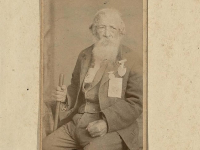 Mounted photograph of Jordan Noble, ca. 1886. Jordan Noble, at around 87 years of age, sits for a full portrait in civil clothes, two medals of honor pinned to chest