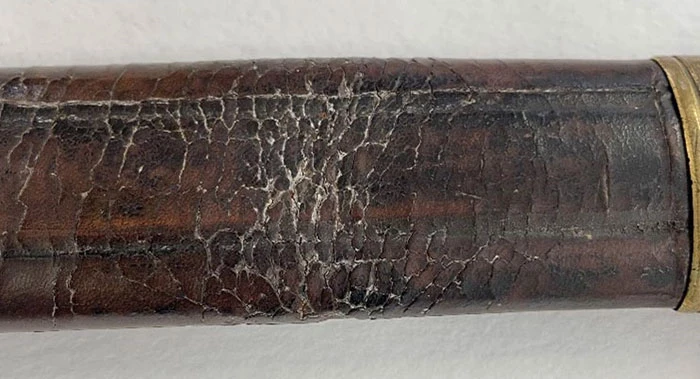 White residue in the cracks of a leather sword scabbard. The residue is polishing compound that was used to clean the adjacent brass components but was inadvertently wiped onto the leather.