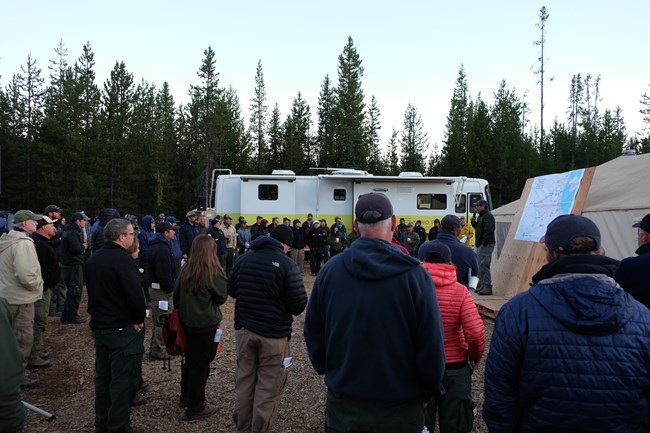 Morning briefing. A group gathered around a person near a map.