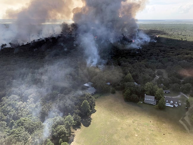 Aerial view of smoke rising from a forested area near houses. Aerial view of smoke rising from a forested area near houses.