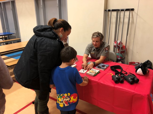 A little boy and adult look at a picture of a bird that a ranger points to.