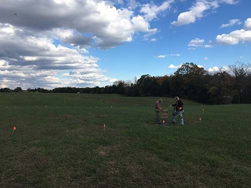 Clayton Field 2017 Two people use archeological investigation tools in open field.