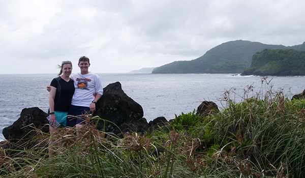 A man and woman stand at point overlooking the ocean.