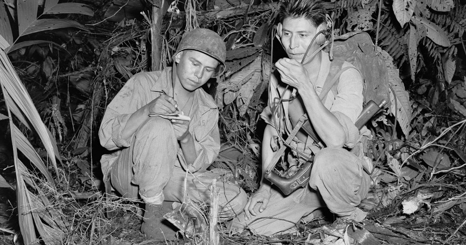 Two military men crouch in the jungle in World War II
