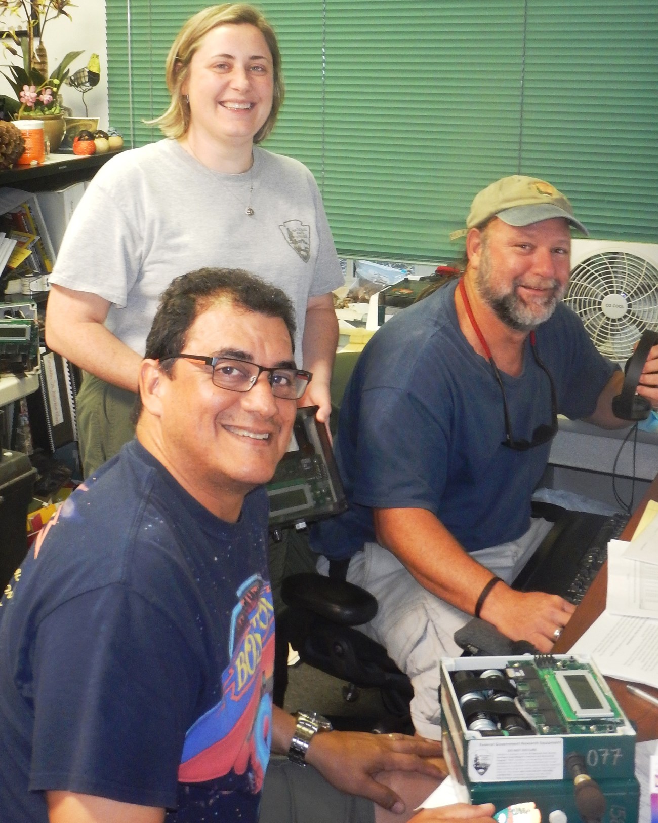Collaborating with the South Florida/Caribbean Network. Two men seated, a woman stands behind them.