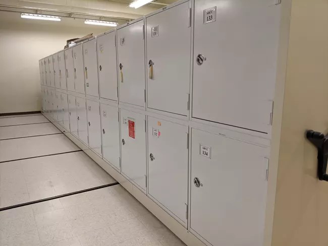 Collection storage at the Alaska Regional Curatorial Center. These hold important materials gathered by scientists, archeologists, and other professionals. Collection storage lockers along a white floor and bright lights.