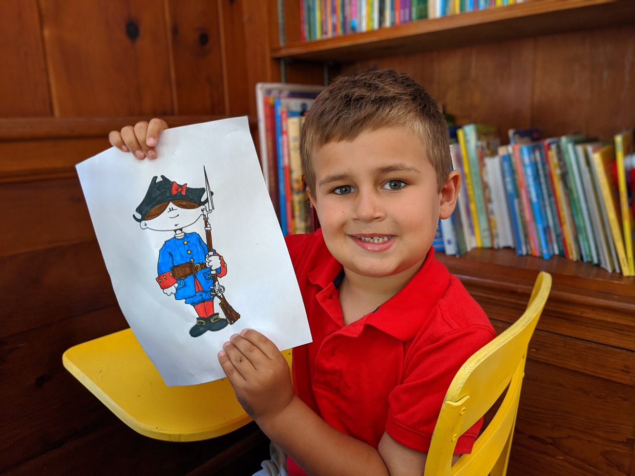 Young boy with a coloring page of a cartoon fort soldier.