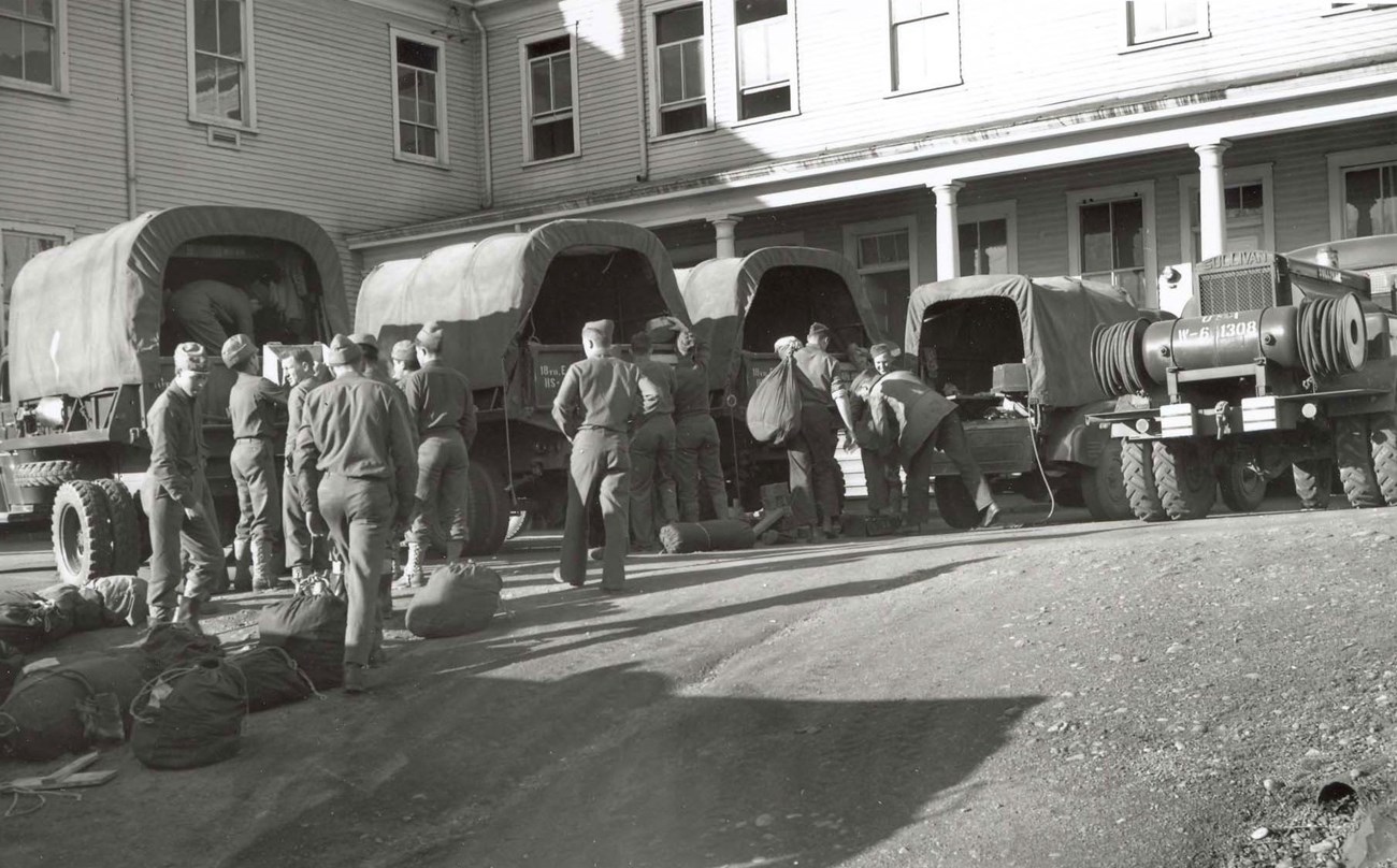 18th Engineers at Vancouver Barracks A black and white photo shows soldiers in WW2 uniforms loading supplies into covered trucks. Behind them is a two-story building with a porch.