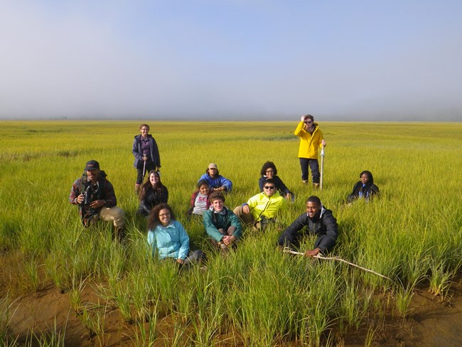 students stand in a meadow and listen to an instructor