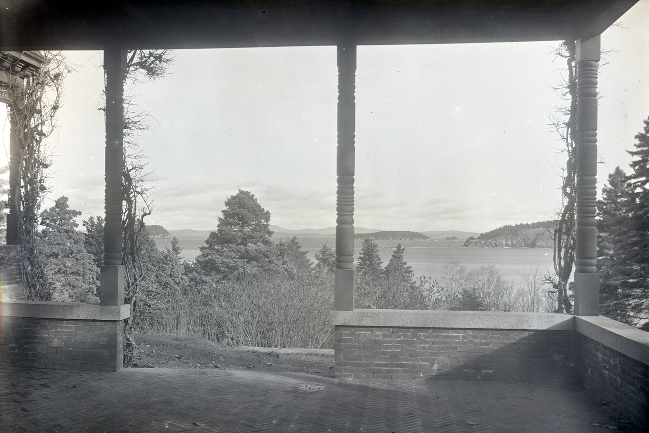 View from a covered patio across trees in foreground of an open harbor and islands in the distance