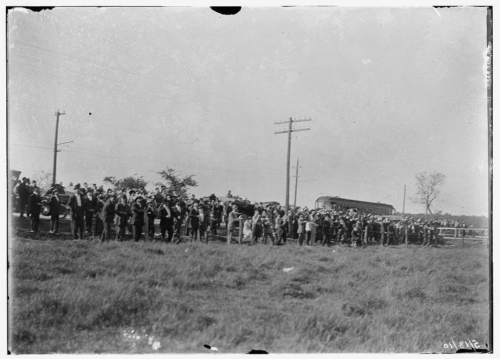 Large crowd of spectators gathered at the edge of a field at Simms Station, Dayton, Ohio, where a series of flights were conducted from May through July, just after the opening of the Wright Flying School. A trolley car is visible in the background