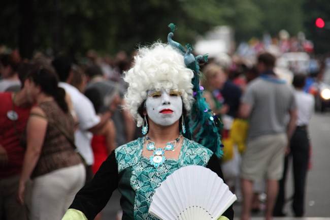 A person with white face, white wig, and opulent blue-green gown