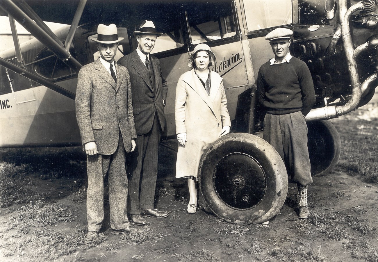 black and white photo of four people standing next to a bus