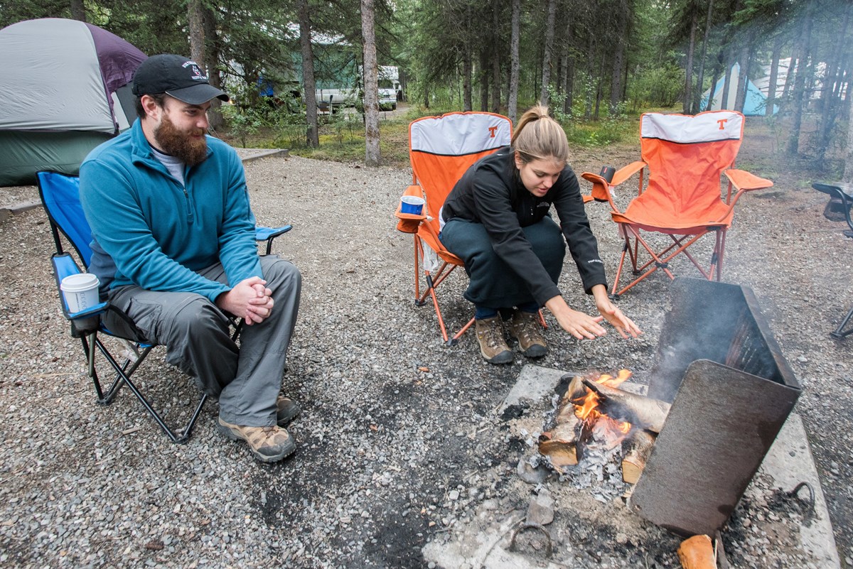 man and woman sit by small campfire