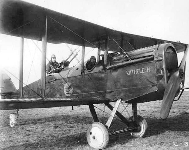 Biplane with pilot and gunner parked in a field