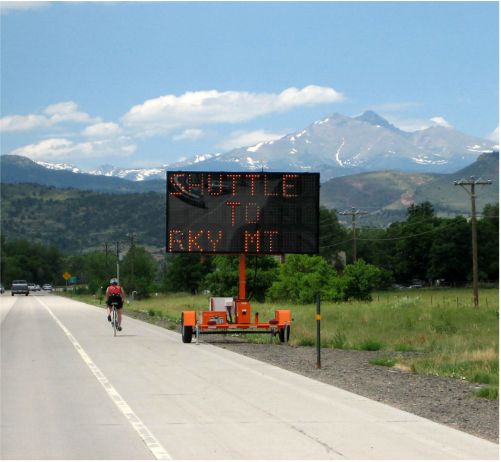 a dynamic message board sign along the side of a road, mountain in distance