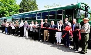 Line of people hodling a red ribbon in front of a green bus