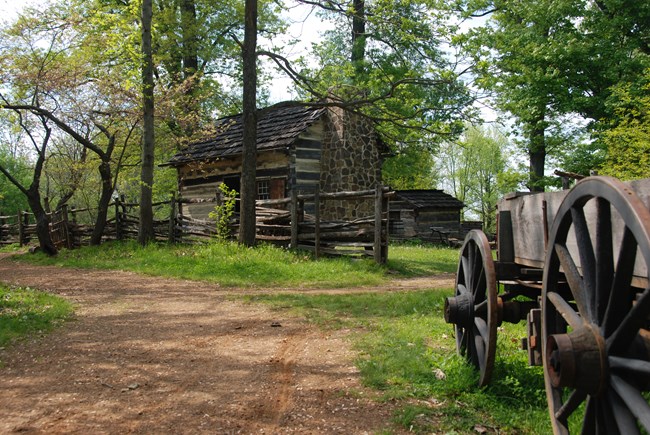 wagon sits beside tree lined trail leading to log cabin