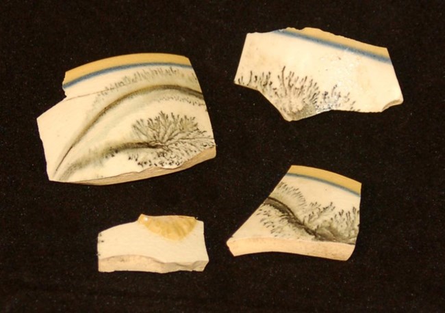 Four ceramic fragments with yellow and blue borders and a black mochaware decoration on a white band in the center.