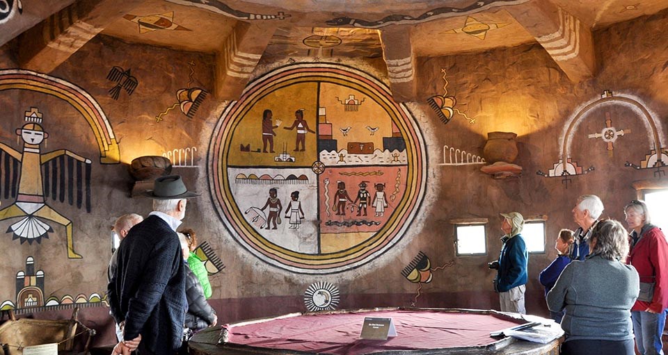 a small group of people are looking at wall murals of Hopi Indian designs within a room in a circular tower.