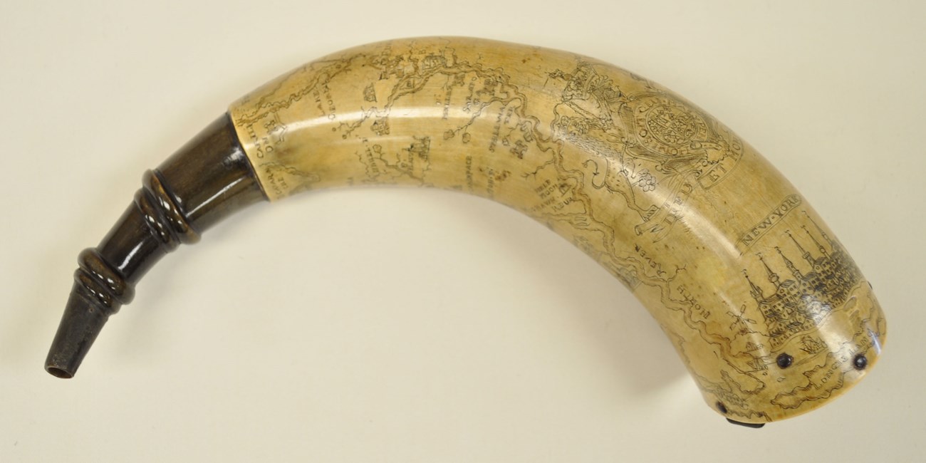 A profile view of a powderhorn with intricate etching on it.