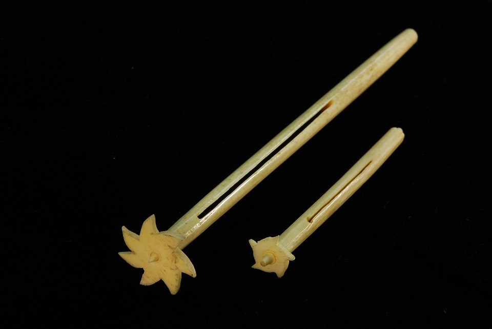 Photo of two long cylindrical rollers, one longer than the other. Each has a pinwheel-shaped piece on one end.