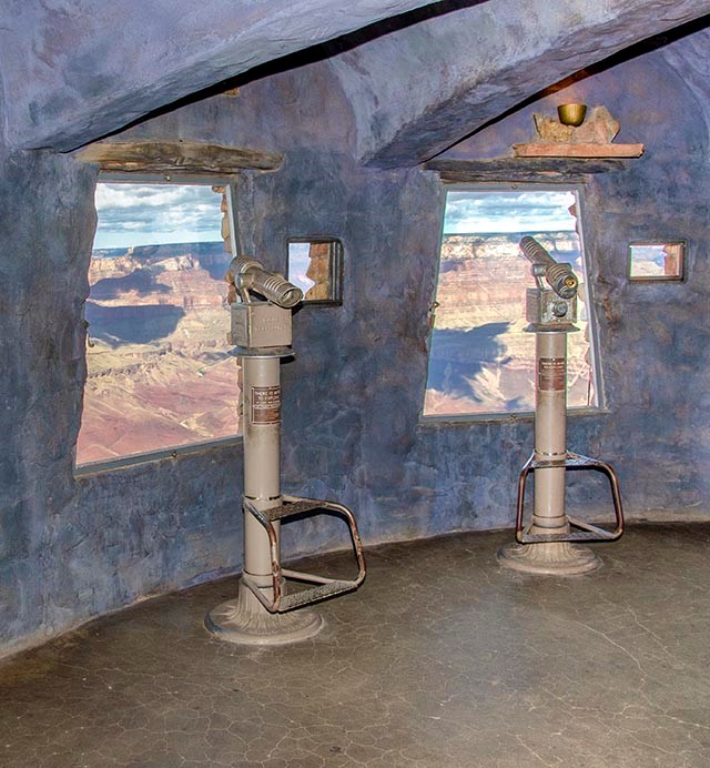 a small circular room with bluish concrete walls with pay telescopes in front of  large windows looking out on a colorful canyon landscape