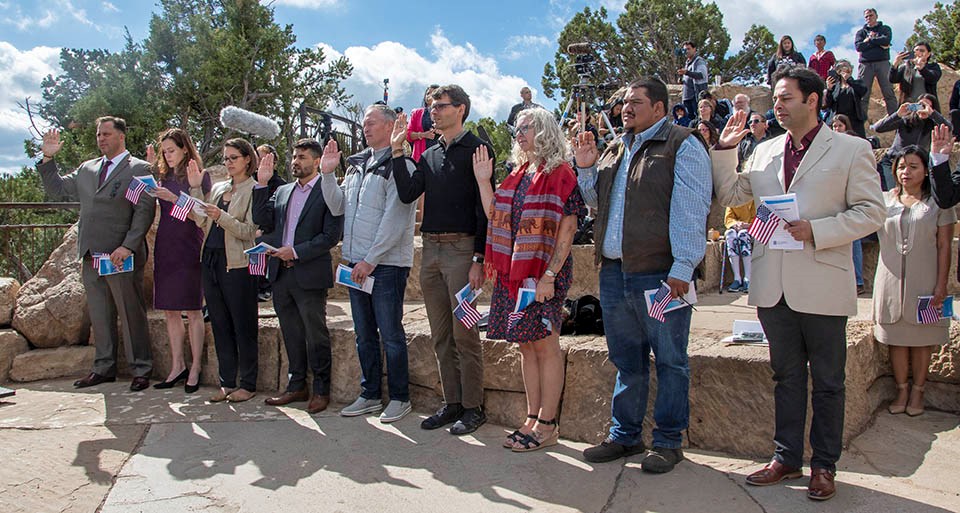 New citizens taking their oath of allegiance during a naturalization ceremony hosted by Grand Canyon National Park 10 individuals holding small American flags are raising their right hands and taking an oath of allegiance.
