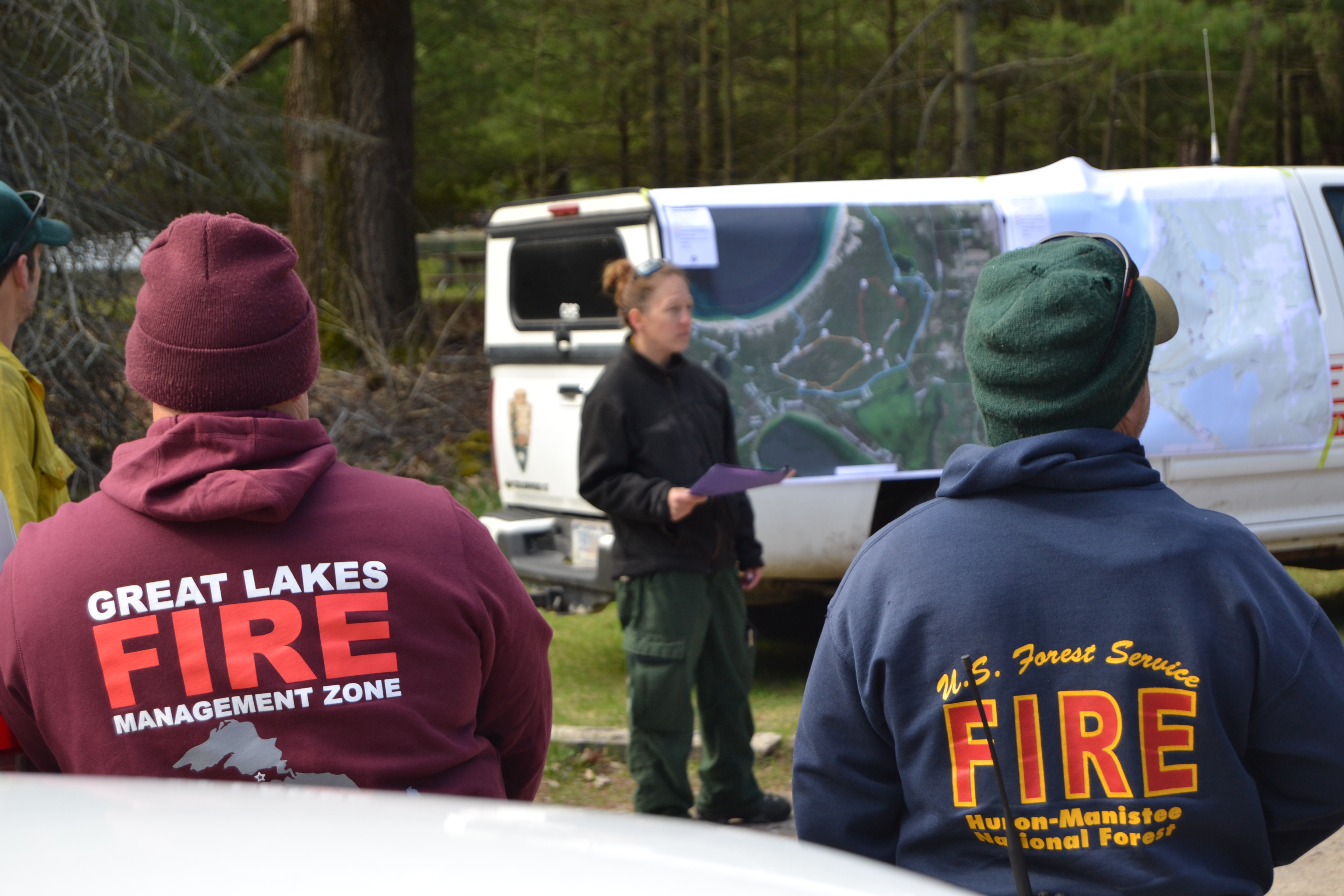 Firefighters listening to briefing from Burn Boss standing in front of map.