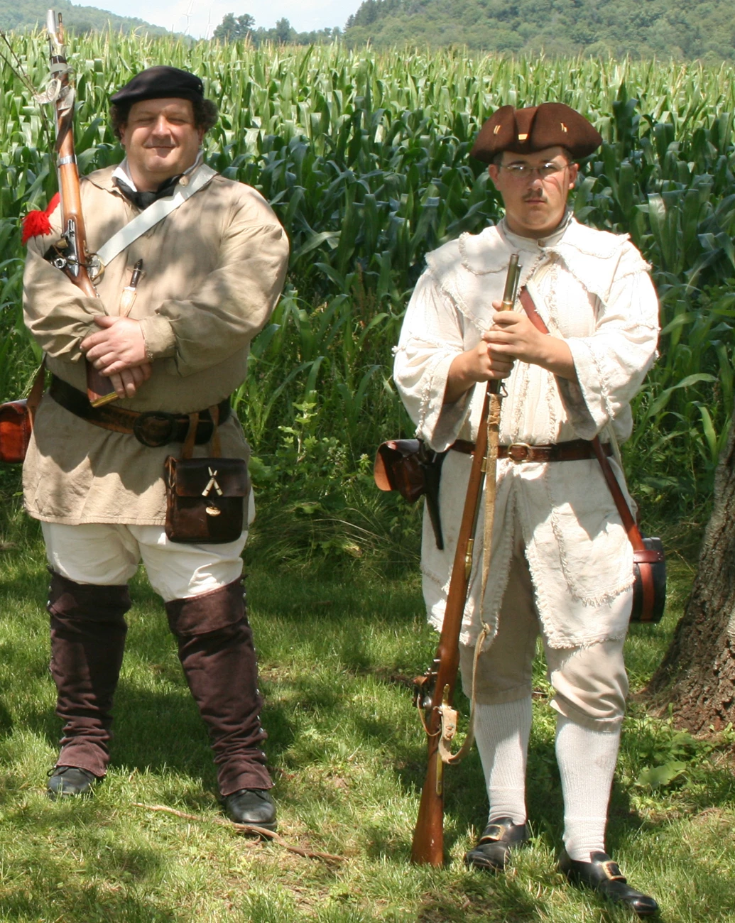 Ranger Dael and son 2 people in Continental Soldier uniforms stand with muskets ready under green trees.