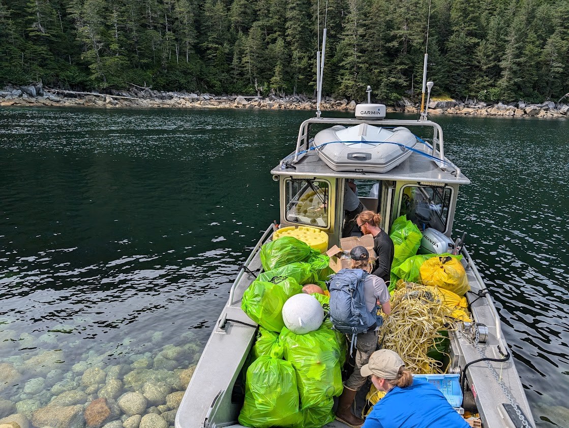 Three people move trash bags onto a boat