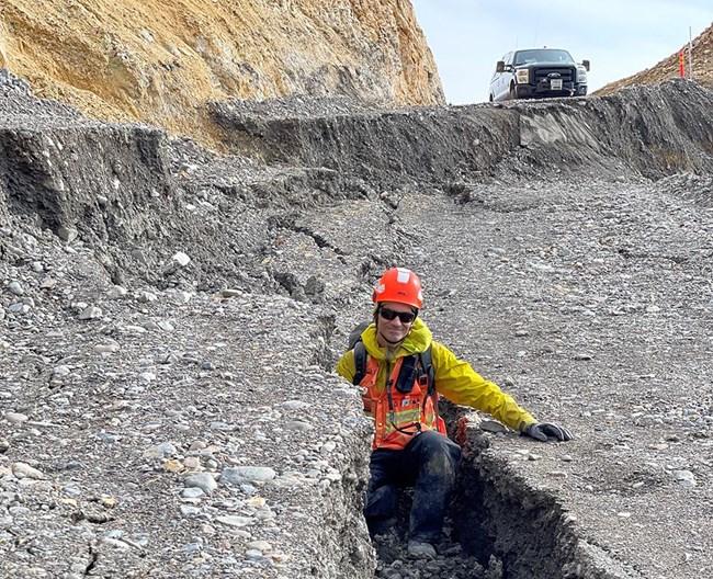 A man stands in a deep crack in a road.