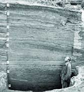 Many Layers of Occupation Man stands in front of rock wall showing many layers of occupation at Onion Portage excavation site (1960s).