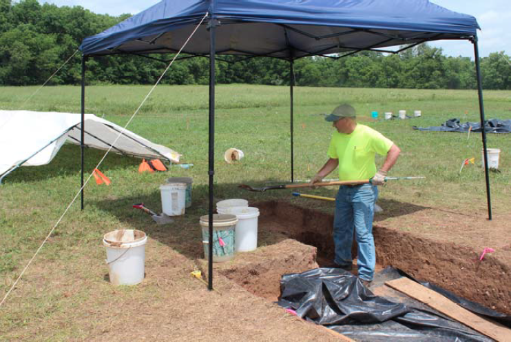 Dr.Timothy Schilling at HMG project site A man using a shovel to move dirt into buckets under a blue tent