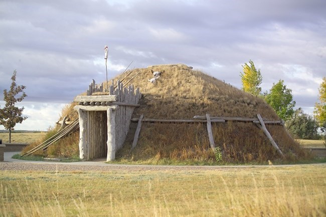 Short grass and sod form a dome, supported by a frame of timbers with a doorway framed by vertical timbers.