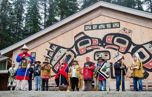 Tlingit tribal members standing outside a building decorated with traditional carving artwork