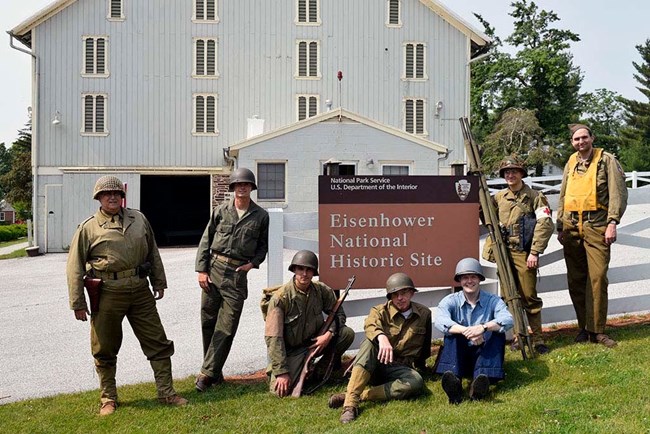 Men in World War II uniforms pose by a park sign Men in World War II uniforms pose by a park sign