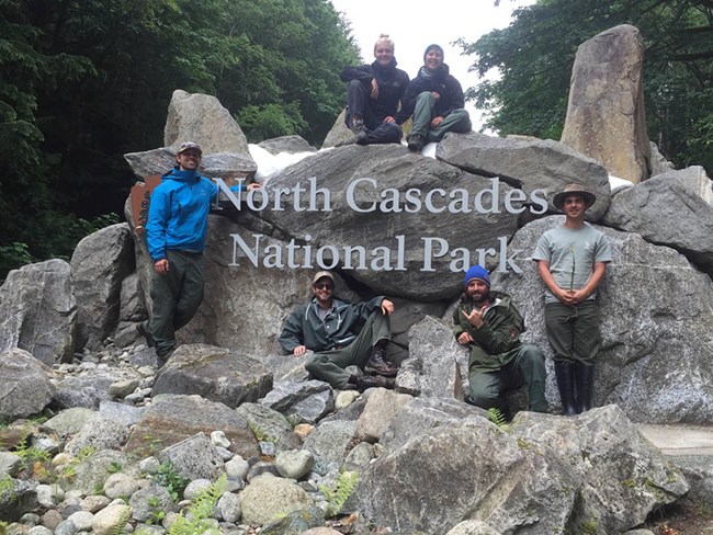 Exotic Plant Management Team at North Cascades Group posing for a photo at an entry sign for North Cascades National Park
