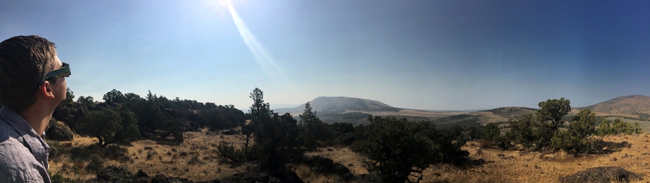 Rear view of a man wearing eclipse glasses looking up at sky with panoramic landscape