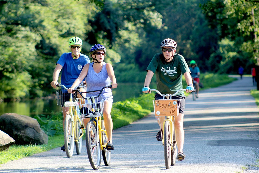 Three people cycle down a trail next to a river.