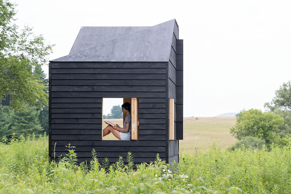 A person sit and writes in an open mobile studio in a meadow.