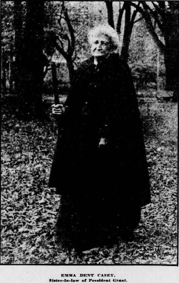 Elderly woman wearing a black cloak, carrying a walking cane and standing in woods