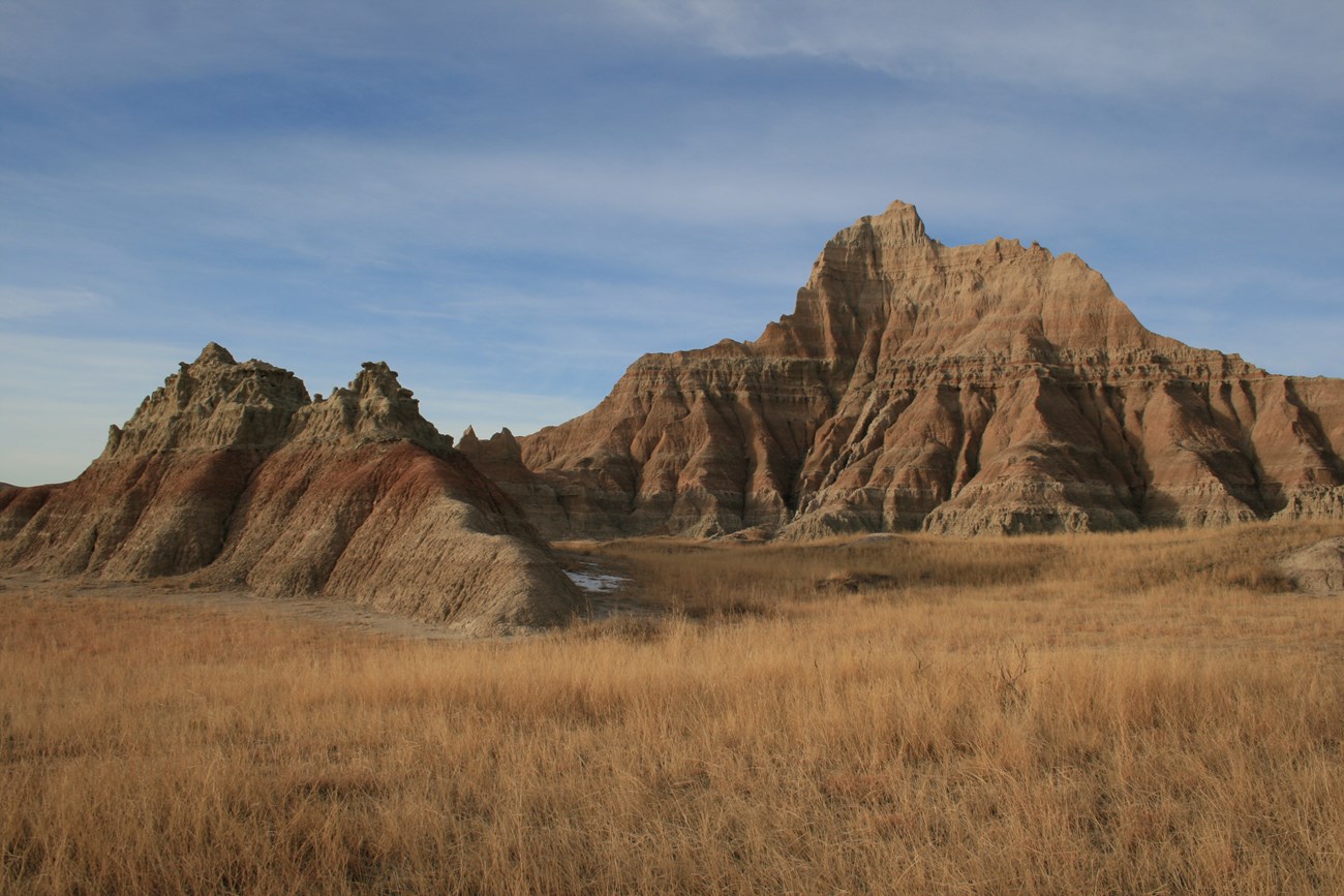 Badlands Formations and Prairie Grasses Near Ben Reifel Visitor Center Brown, rocky mountain formation against a blue sky