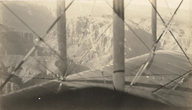 Black and white photo looking out over the wing of a biplane. Beyond is a view of the Grand Canyon.