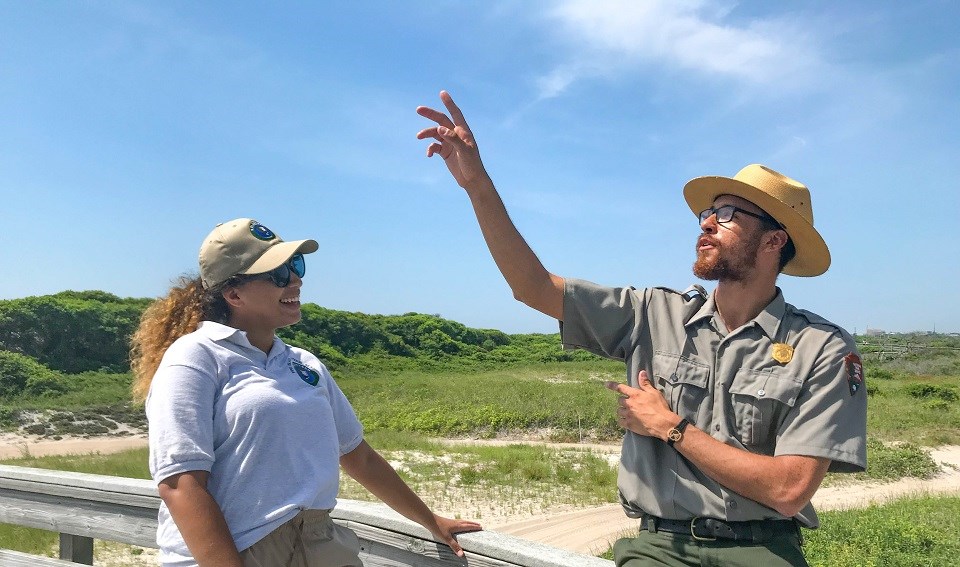 NPS Volunteer and Ranger talking on a boardwalk over beach dunes