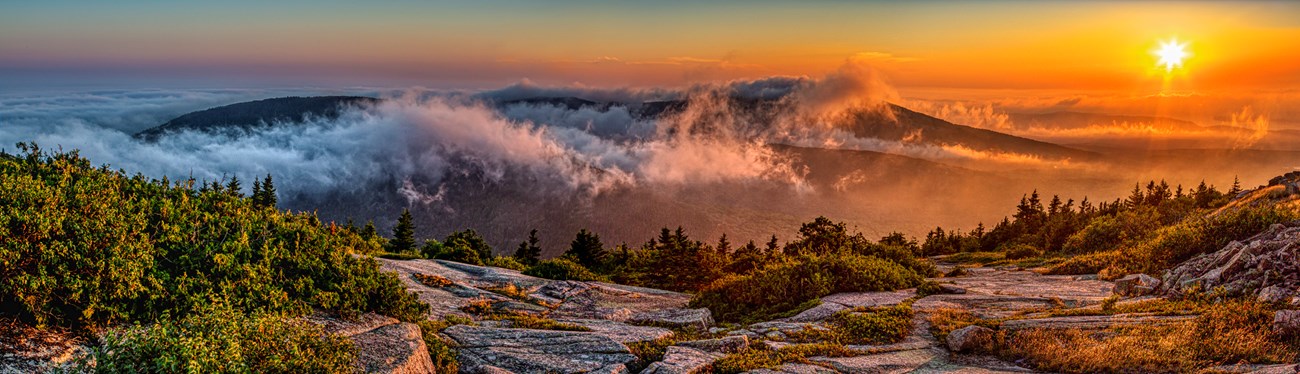 Landscape photograph of sunrise along the North Atlantic coastline with clouds drifting among mountain summits.