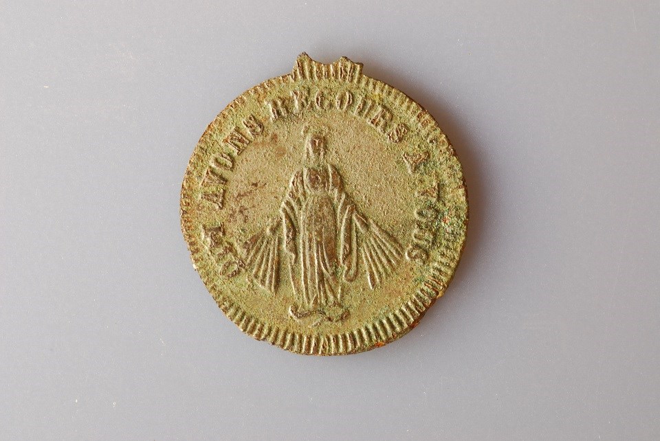 Photo of the front of a small medallion with the image of the Virgin Mary surrounded by words in French.